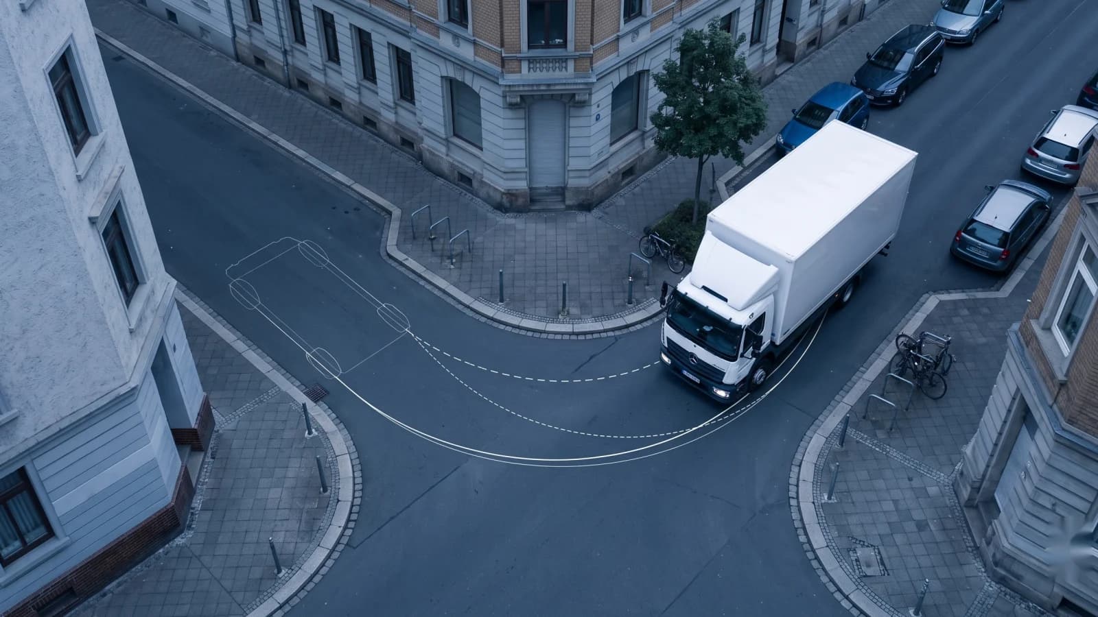 Aerial view of a white box truck turning at a narrow European street corner, with overlay curves comparing an instant steering arc to a smooth rate-limited path