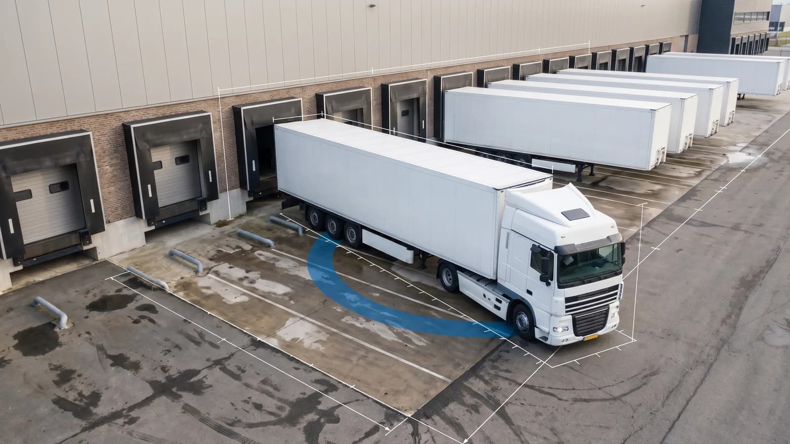 Witte trekker met oplegger die schuin achteruit een laaddock van een distributiecentrum insteekt, met een blauwe rijcurveband onder de binnenwielen van de oplegger